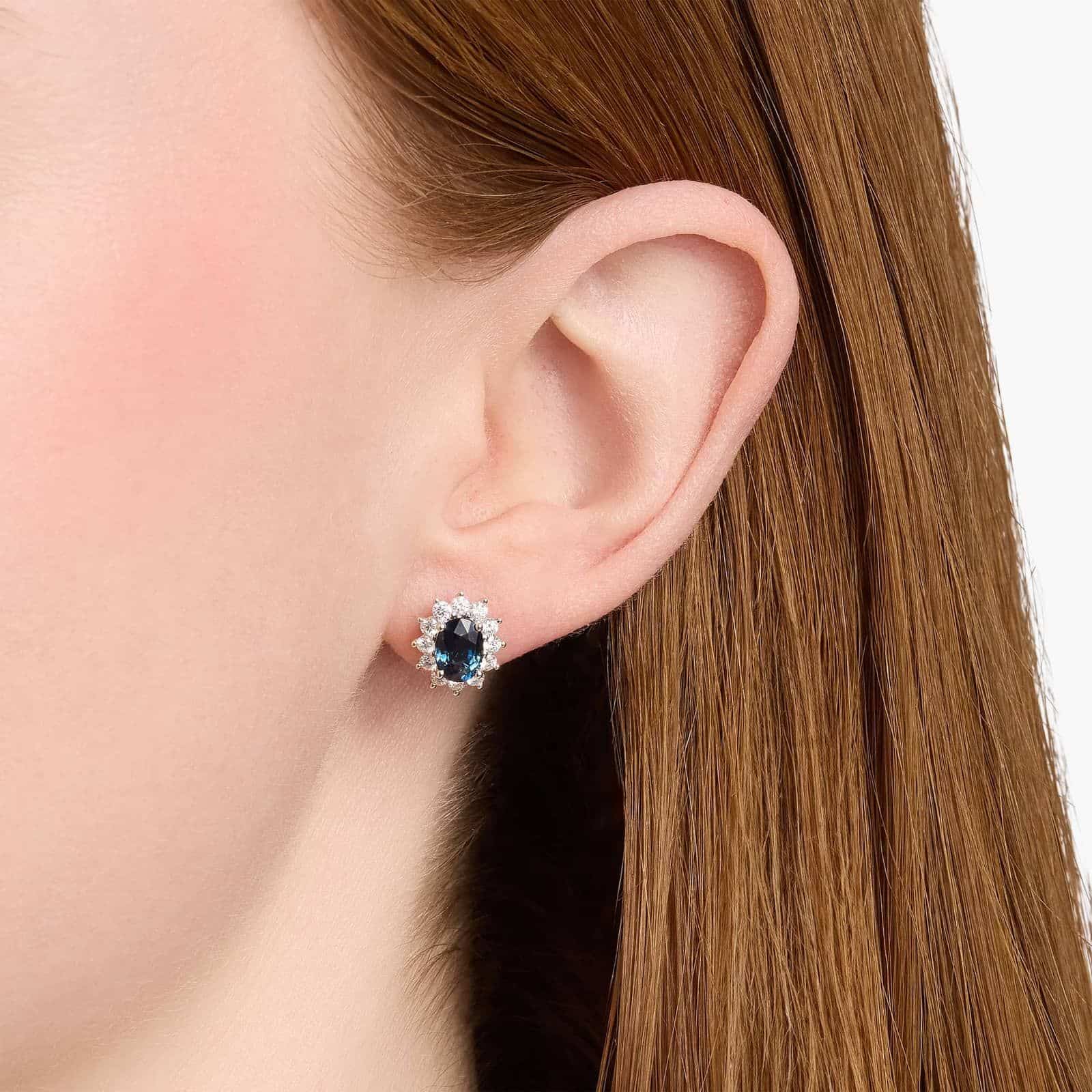 An 18K White Gold White Gold and Sapphire Earrings set featuring two 7x5 mm Oval Blue Sapphires surrounded by a 0.72 CTW Round Diamond Halo, secured with Push Backs.