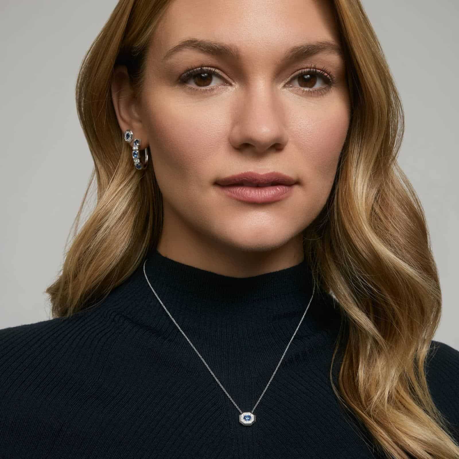 14K white gold blue sapphire pendant necklace featuring a 0.48 carat oval blue sapphire center stone and a pavé diamond halo on an 18-inch rolo chain.